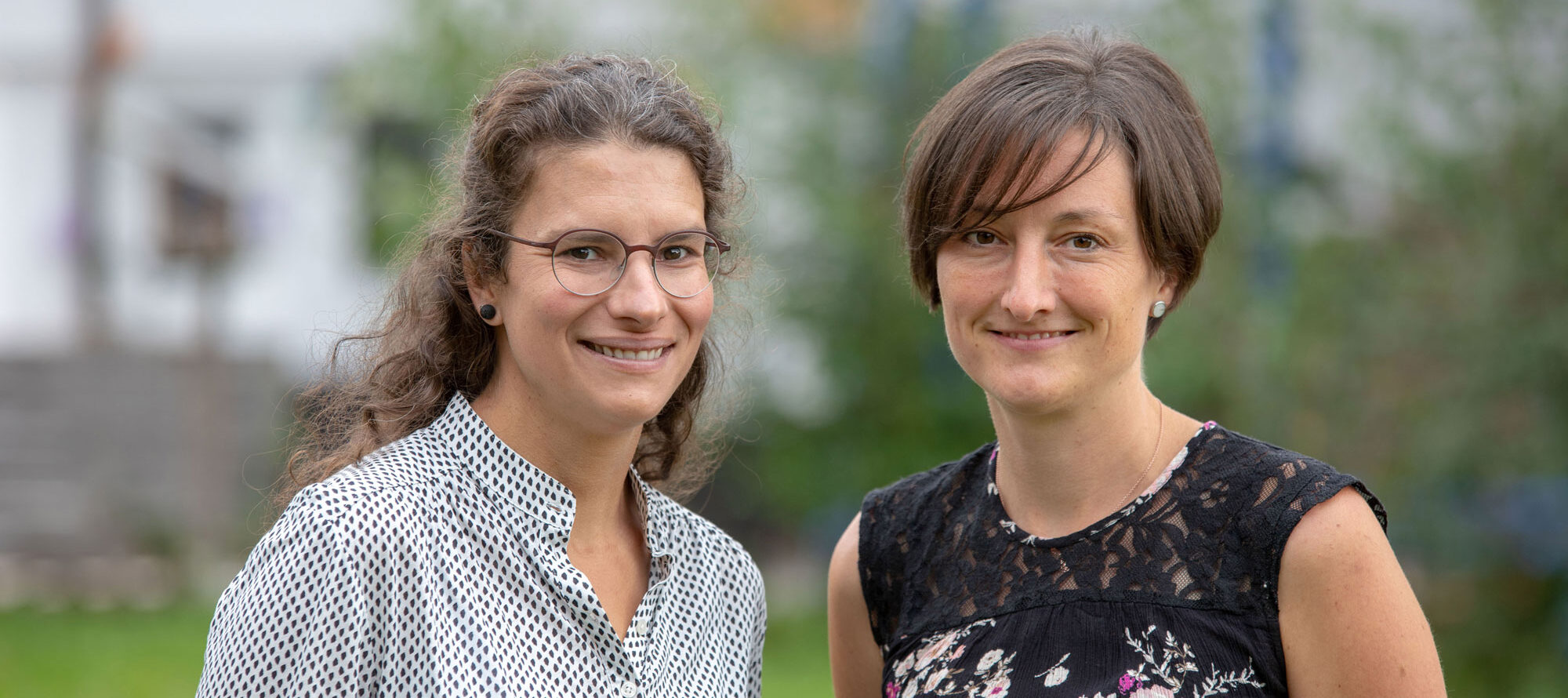 Portrait der Praxisleitung: Anja Engesser (links mit Brille und gemusterter Bluse) und Ramona Marx (rechts mit dunklem Spitzenoberteil) blicken sympathisch in die Kamera.